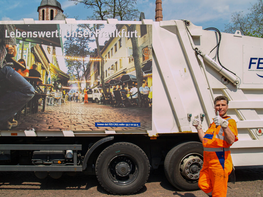 Man in orange suit giving thumb up in front of a garbage truck